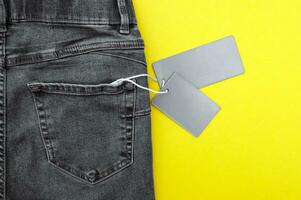 Flat lay, detail of black jeans, blank grey labels on yellow background. photo