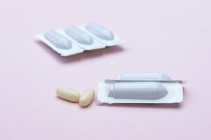 Gynecological medicines for women's health in form of suppository, capsules on pink background. photo