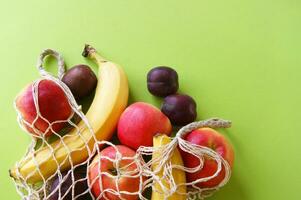 Red apples, bananas, plums and string bag on a bright green background. photo