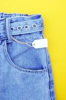 Flat lay, detail of denim jeans, blank white labels on yellow background. photo