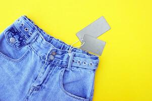 Flat lay, detail of denim jeans with blank gray label on yellow background. photo