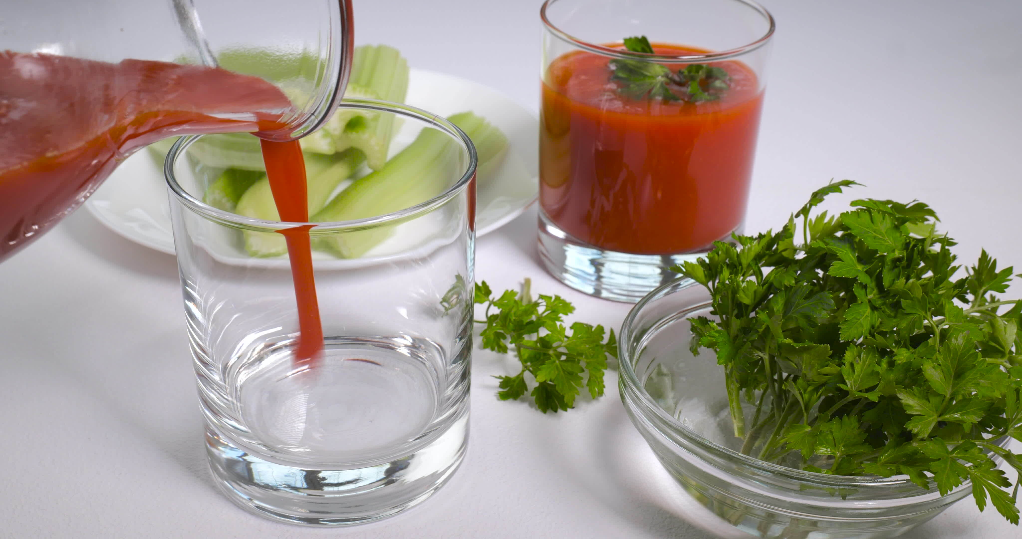 Pouring organic freshly squeezed tomato juice into a glass. Celery and