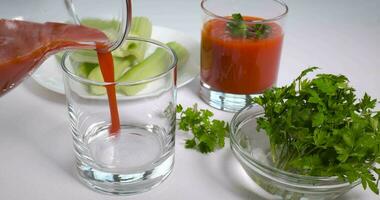 torrencial orgánico recién exprimido tomate jugo dentro un vaso. apio y perejil en un blanco mesa. sano y vegetariano comida concepto. ultra 4k video