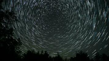 Time lapse of comet-shaped star trails over the forest in the night sky. Stars move around a polar star. 4K video