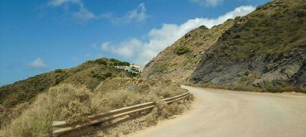 Winding road leading up a hill with sparse vegetation under a clear blue sky. photo