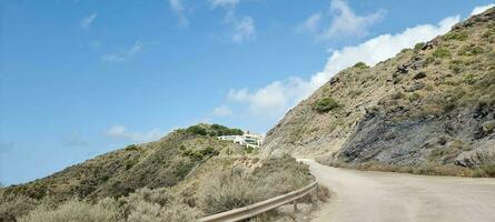 Winding road leading to a hillside house with clear blue skies and sparse vegetation. photo