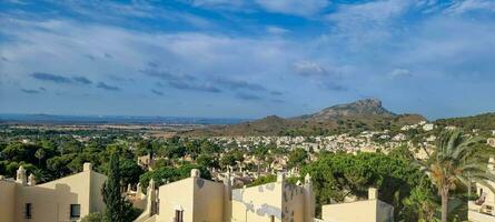 Panoramic view of a Mediterranean town with houses in the foreground and a mountain in the background under a blue sky. photo