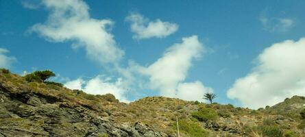 Scenic view of a rocky hillside with sparse greenery under a blue sky with fluffy clouds. photo