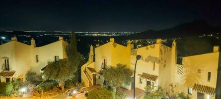 Night view of a traditional village with illuminated buildings against a mountainous backdrop. photo