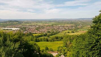 Panoramic view of a lush valley with residential areas, green fields, and trees under a clear blue sky. photo