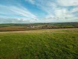 Rural landscape with green fields under a blue sky with wispy clouds, distant village in the backdrop. photo