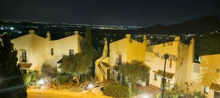 Nighttime view of traditional houses with illuminated streetlights against a mountain backdrop. photo