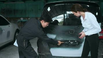 A young Caucasian woman explains about her car problems to mechanic man in auto repair shop video