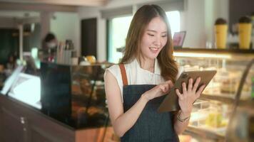 ett asiatisk kvinna entreprenör använder sig av läsplatta kontroll stock eller försäljning inkomst i modern kaffe affär , begrepp små företag video
