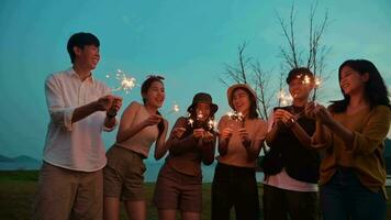 grupo de joven asiático personas son disfrutar cámping , jugando bengala en natural cámping a crepúsculo video
