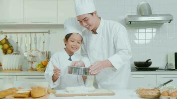 joven asiático padre y su hijo vistiendo cocinero uniforme horneando juntos en cocina a hogar video