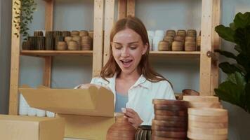 un joven bonito mujer empresario comprobación y embalaje arte productos de venta a clientes en su tienda video