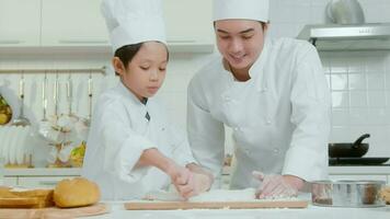joven asiático padre y su hijo vistiendo cocinero uniforme horneando juntos en cocina a hogar video