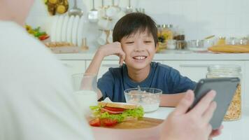 giovane asiatico padre e il suo figlio utilizzando digitale tavoletta godendo insieme nel cucina a casa video