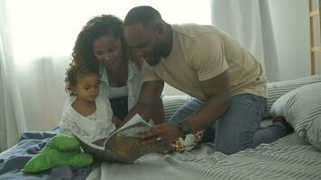 Happy African American Parents with  little daughters playing , reading book on the bed in bedroom at home, happy family concept video