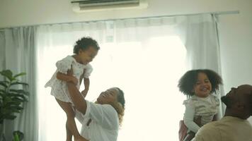 feliz africano americano pais com pequeno filhas jogando em a cama dentro quarto às lar, feliz família conceito video