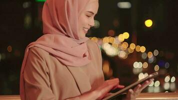 una joven mujer de negocios musulmana está usando una tableta en una ciudad moderna por la noche, concepto de estilo de vida de tecnología empresarial video