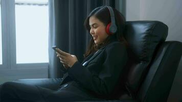 Young relaxing business woman using smartphone and listening to music in modern office. video