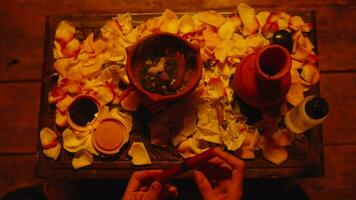 a woman is putting lipstick among roses and a ritual jug on a wooden table video