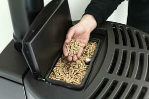 Pellet stove, man holding granules in his hand above a modern black stove photo