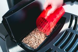 Close-up on pellets, black domestic pellet stove, man loading by hand granules with a red 3 d printed cup photo