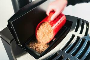 Close-up on pellets, black domestic pellet stove, man loading by hand granules with a red 3 d printed cup photo