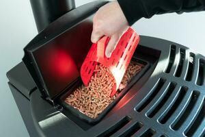 Close-up on pellets, black domestic pellet stove, man loading by hand granules with a red 3 d printed cup photo