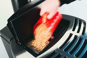 Close-up on pellets, black domestic pellet stove, man loading by hand granules with a red 3 d printed cup photo