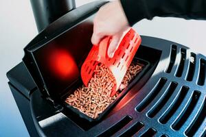 Close-up on pellets, black domestic pellet stove, man loading by hand granules with a red 3 d printed cup photo