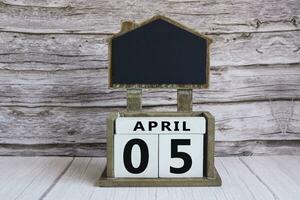 Chalkboard with April 05 date on white cube block on wooden table. photo