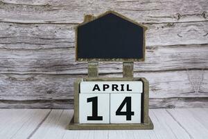 Chalkboard with April 14 date on white cube block on wooden table. photo