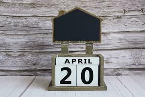 Chalkboard with April 20 date on white cube block on wooden table. photo