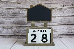 Chalkboard with April 28 date on white cube block on wooden table. photo