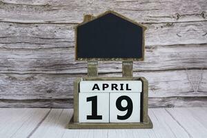 Chalkboard with April 19 date on white cube block on wooden table. photo