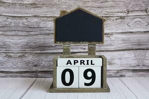 Chalkboard with April 09 date on white cube block on wooden table. photo