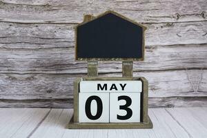 Chalkboard with May 03 date on white cube block on wooden table. photo