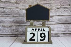Chalkboard with April 29 date on white cube block on wooden table. photo