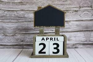 Chalkboard with April 23 date on white cube block on wooden table. photo