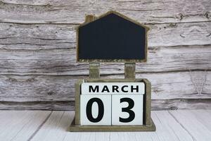 Chalkboard with March 03 date on white cube block on wooden table. photo