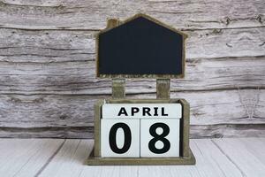 Chalkboard with April 08 date on white cube block on wooden table. photo