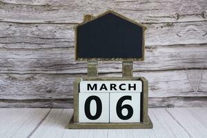 Chalkboard with March 06 date on white cube block on wooden table. photo