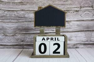 Chalkboard with April 02 date on white cube block on wooden table. photo