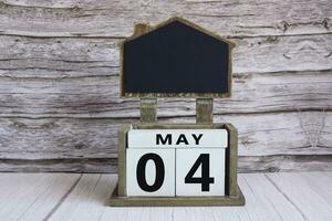 Chalkboard with May 04 date on white cube block on wooden table. photo