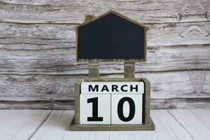 Chalkboard with March 10 date on white cube block on wooden table. photo