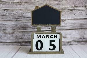 Chalkboard with March 05 date on white cube block on wooden table. photo